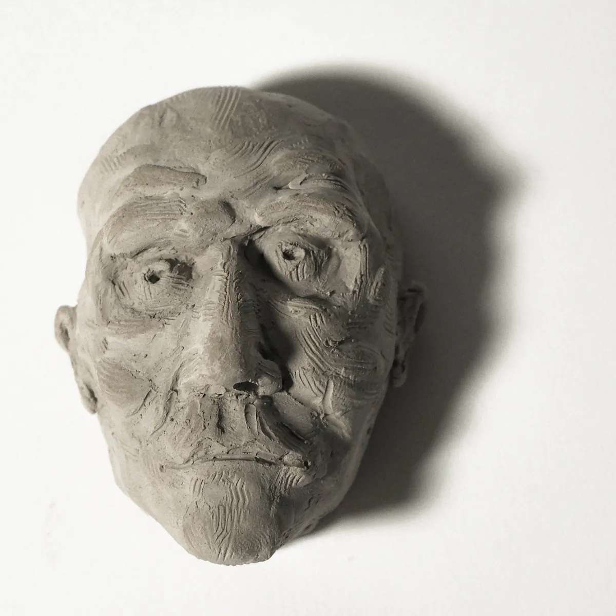 A stoneware head of an elderly man seen from above, deep-set eyes and heavily textured, wrinkled skin.